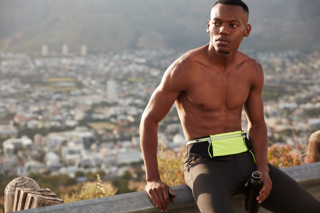 Countryside healthy active lifestyle concept. Concentrated ethnic man with muscular body, holds sport bottle filled with water, takes break after sprinting, ready for running marathon, joggs outside