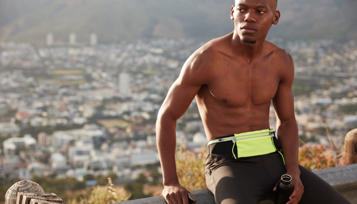 Countryside healthy active lifestyle concept. Concentrated ethnic man with muscular body, holds sport bottle filled with water, takes break after sprinting, ready for running marathon, joggs outside